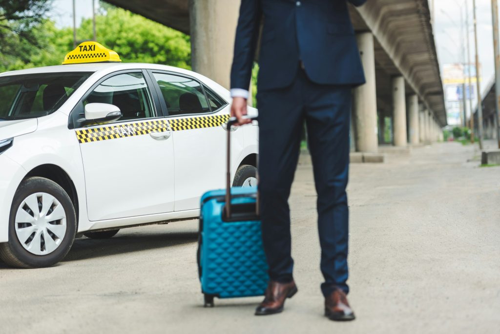 cropped shot of man in suit holding suitcase while standing near taxi cab