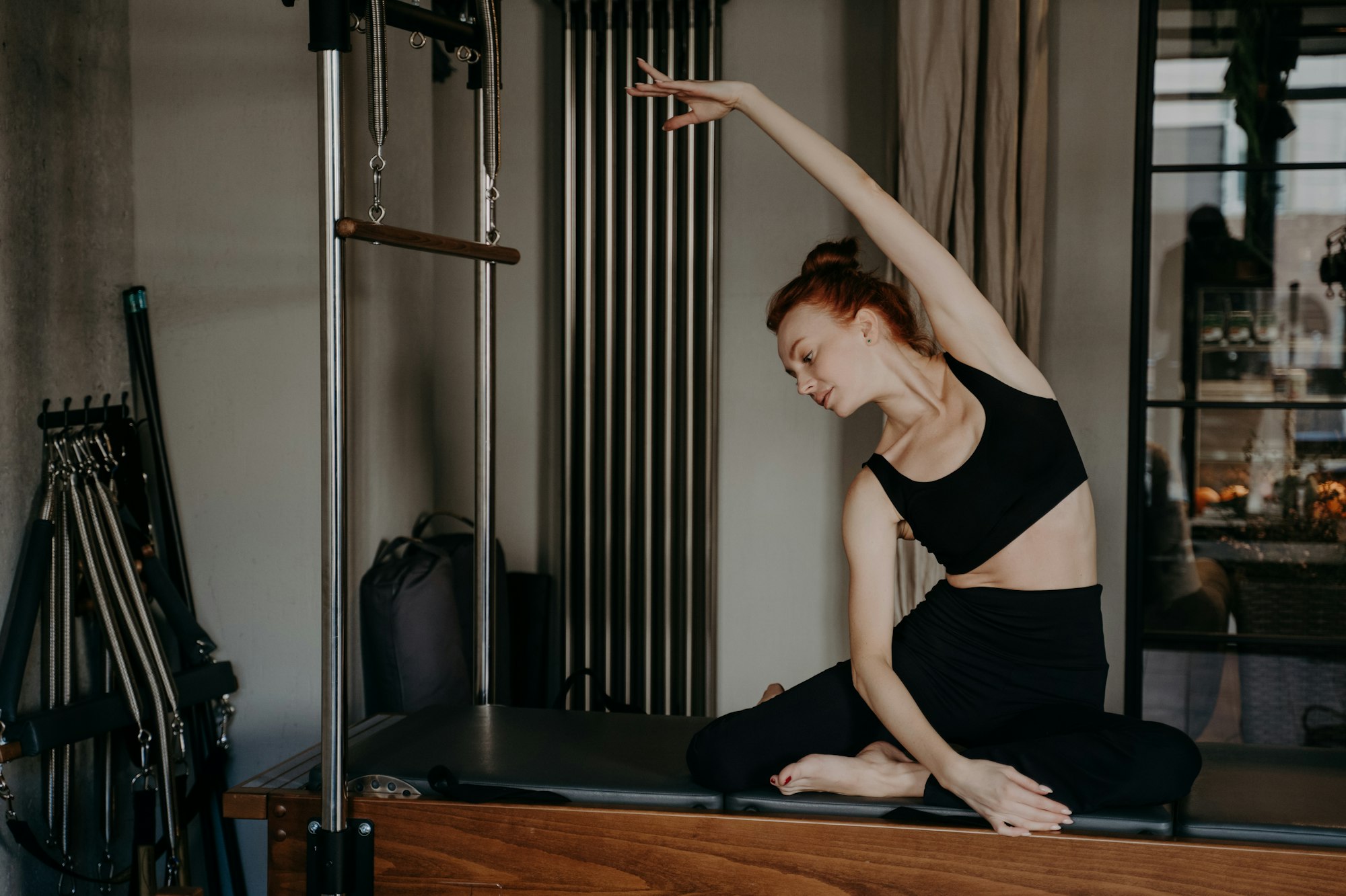 Young ginger woman doing pilates exercises with reformer