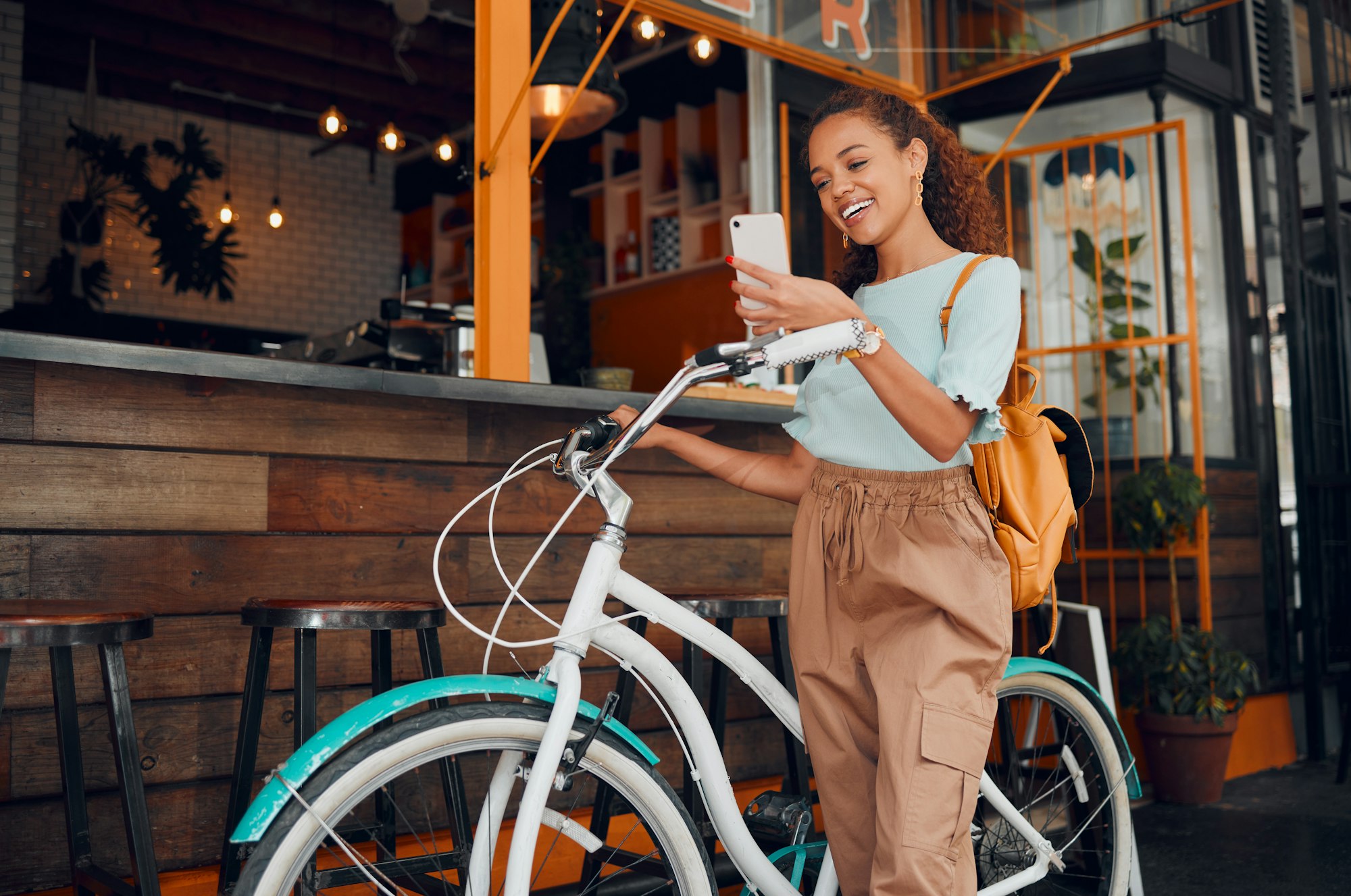 Woman, happy and bike with phone at cafe on travel in city with bag. Black woman, smartphone and sm